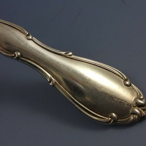 May include: Close-up of the handle of a silver fork with an ornate design. The handle is smooth and shiny.