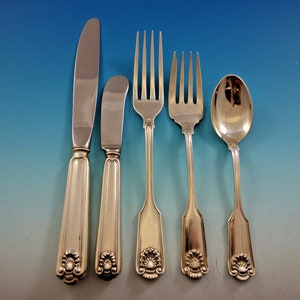 May include: A set of five silver-plated flatware pieces, including a knife, butter knife, fork, and two spoons. The handles are decorated with a shell design.