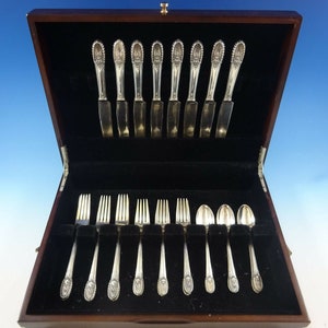 May include: A wooden box with a black velvet interior containing a set of silverware. The silverware includes forks, knives, and spoons. The silverware is arranged in rows in the box.