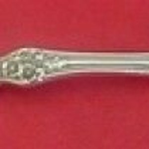 May include: A silver serving fork with a decorative floral pattern on the handle and a two-pronged end. The tines have a twisted design. The fork is displayed against a red background, showcasing its intricate details.