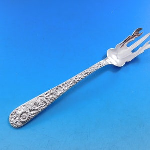 May include: A silver serving fork with an ornate floral design. The fork has three tines and a long, slender handle.