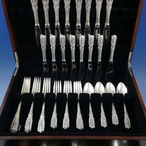 Puede incluir: Una caja de madera con un interior de terciopelo negro que contiene un juego de cubiertos de plata. El juego incluye cuchillos, tenedores, cucharas y piezas para servir. Los cubiertos son ornamentados y presentan un dise&ntilde;o floral.