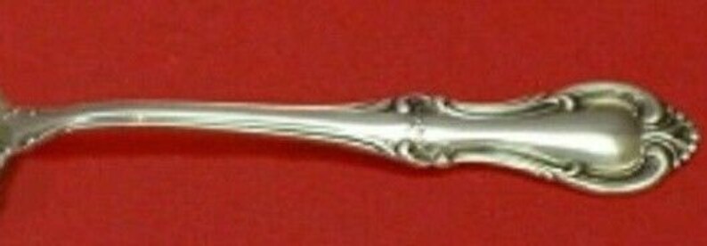 Puede incluir: Una cucharita de plata con un mango curvo adornado.