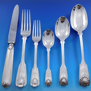 May include: A set of six silver-plated flatware pieces, including a knife, fork, and spoon. The handles are ornate and feature a shell design. The pieces are arranged on a blue background.