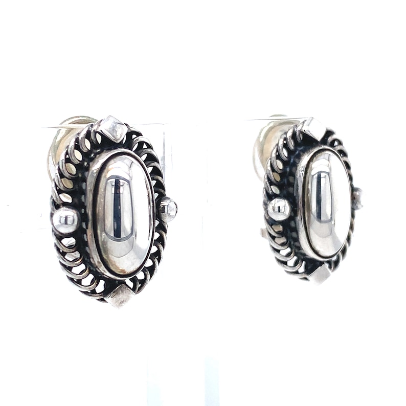 Puede incluir: Un par de pendientes de plata con un dise&ntilde;o ovalado detallado. Los pendientes tienen un acabado liso y pulido y un borde delicado e intrincado.