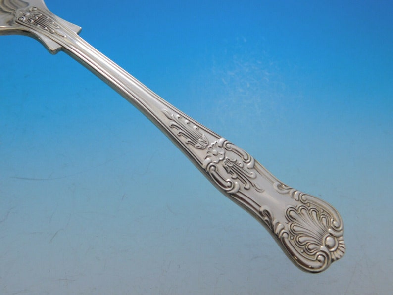 May include: Close-up of the ornate handle of a silver fork. The handle is decorated with a floral design and has a polished finish.