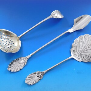 May include: Three silver serving spoons with ornate handles. The spoons have different shapes and designs, including a spoon with a perforated bowl.