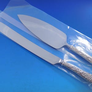 May include: A silver cake knife and server set with ornate handles. The blades are polished and the handles are detailed with a floral design.