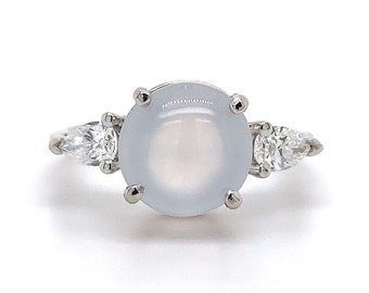 May include: A silver ring with a large, round, light blue gemstone surrounded by smaller, clear gemstones.