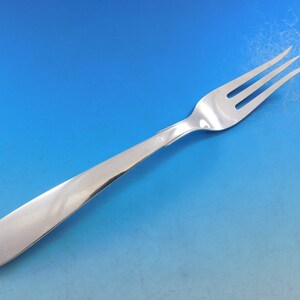 Puede incluir: Un tenedor de plata con un mango largo y delgado y tres dientes. El tenedor est&aacute; sobre un fondo azul.