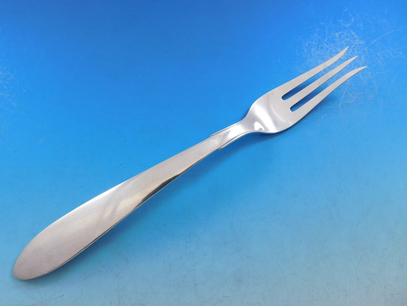 Puede incluir: Un tenedor de plata con un mango largo y delgado y tres dientes. El tenedor est&aacute; sobre un fondo azul.