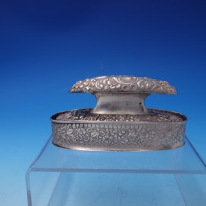 May include: A silver oval-shaped box with a hinged lid. The box and lid are decorated with an intricate floral design.
