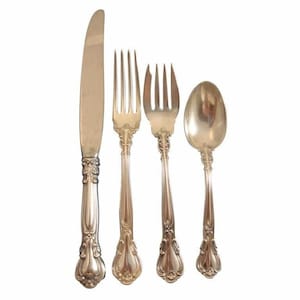 May include: A silver-colored flatware set including a knife, two forks, and a spoon. The handles have an ornate, floral design. The knife is on the left, followed by a fork with three tines, a fork with four tines, and a spoon.