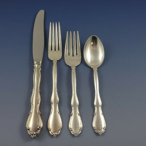 May include: A set of four silver-plated flatware pieces, including a knife, two forks, and a spoon. The pieces have ornate handles with a scalloped design.