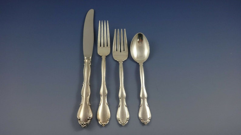 May include: A set of four silver-plated flatware pieces, including a knife, two forks, and a spoon. The pieces have ornate handles with a scalloped design.
