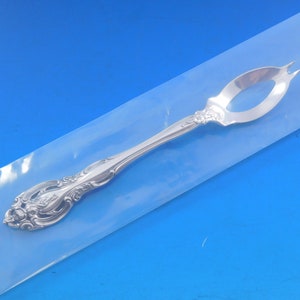 May include: A silver serving fork with an ornate handle and a decorative openwork design. The fork is in a clear plastic bag.