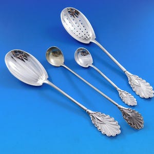 May include: Four silver spoons with ornate handles. The spoons have different shapes, including a slotted spoon and a spoon with a rounded bowl. The spoons are arranged on a blue background.