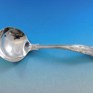 May include: A silver serving ladle with a decorative handle. The ladle has a round bowl and a long, curved handle with an ornate design.