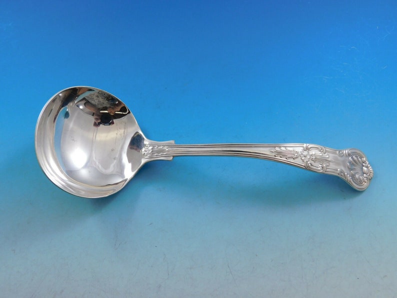 May include: A silver serving ladle with a decorative handle. The ladle has a round bowl and a long, curved handle with an ornate design.