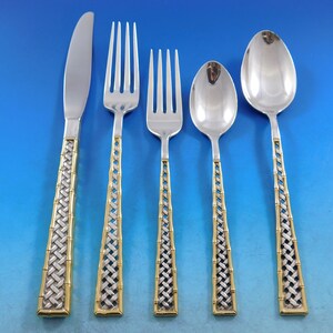 May include: A set of five silver and gold flatware pieces with a woven pattern on the handles. The set includes a knife, two forks, and two spoons.