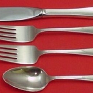 May include: A set of four pieces of silverware: a knife, two forks, and a spoon. The silverware is made of shiny, polished metal and is arranged on a red background. The knife is at the top, followed by the forks and the spoon.