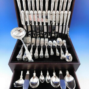 May include: A wooden box with a velvet lining contains a set of silver flatware. The set includes forks, knives, spoons, and a serving spoon. The flatware is arranged in rows in the box.