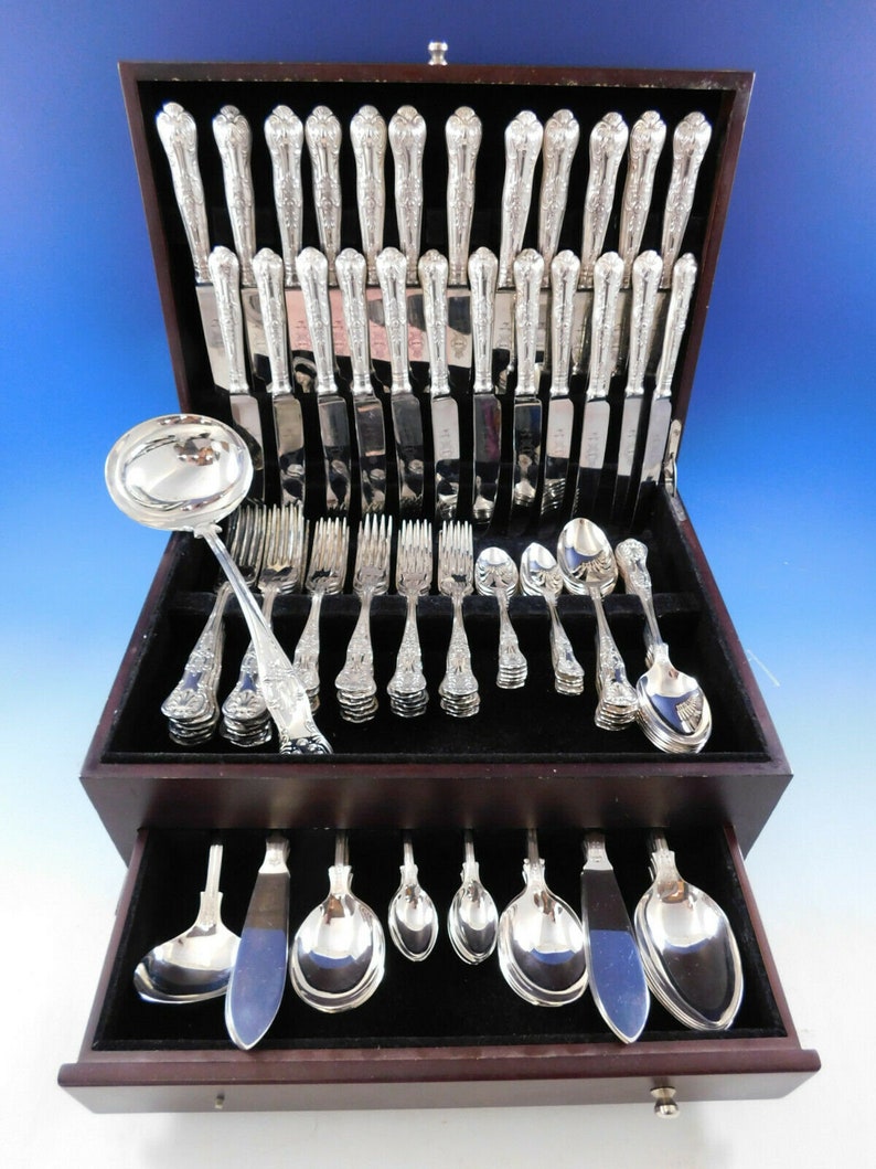 May include: A wooden box with a velvet lining contains a set of silver flatware. The set includes forks, knives, spoons, and a serving spoon. The flatware is arranged in rows in the box.