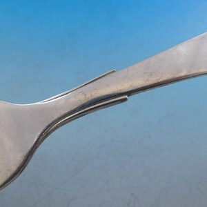 Puede incluir: Primer plano de la parte posterior de un tenedor de plata, que muestra el mango curvo y liso y los dientes.