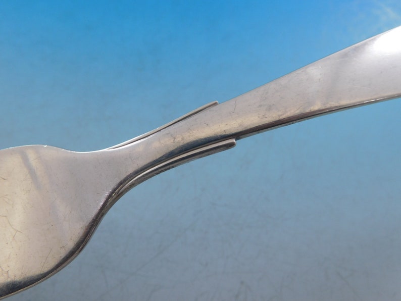 Puede incluir: Primer plano de la parte posterior de un tenedor de plata, que muestra el mango curvo y liso y los dientes.