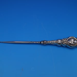 May include: A silver shoe horn with an ornate, floral design on the handle. The handle features a raised, detailed design of a woman's face.