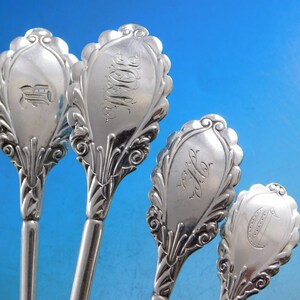 May include: Four silver spoons with ornate handles and engraved initials. The spoons have a decorative, scalloped design and are in excellent condition.