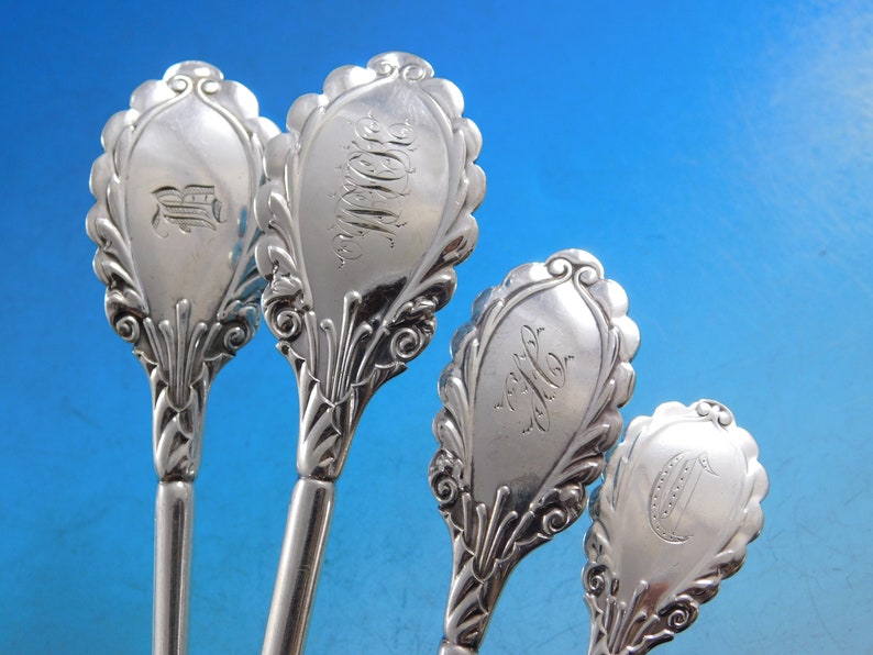 May include: Four silver spoons with ornate handles and engraved initials. The spoons have a decorative, scalloped design and are in excellent condition.