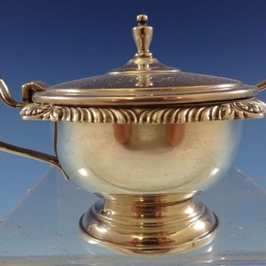 May include: Silver sugar bowl with a lid and a small spoon. The bowl has a rounded body and a pedestal base. The lid has a knob on top.