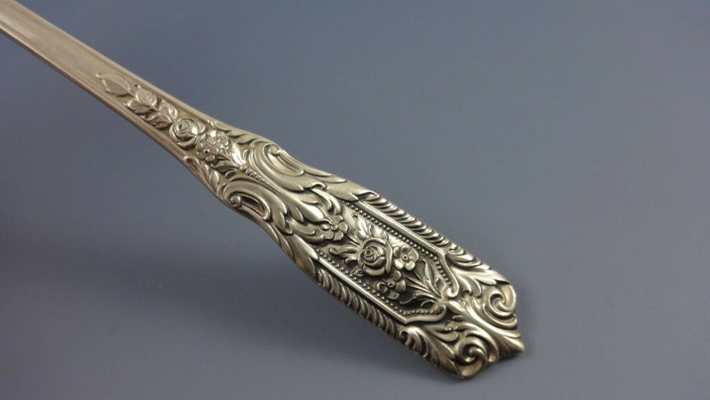 Puede incluir: Primer plano del mango adornado de una cuchara de servir de plata. El mango est&aacute; decorado con un dise&ntilde;o floral, que incluye rosas y hojas.