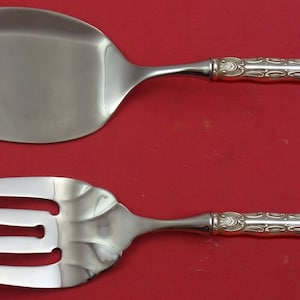 May include: A silver serving set with a knife and fork. The handles are ornate and have a detailed design.