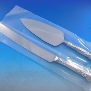 May include: A set of two silver-plated cake knives in a clear plastic bag. The knives have ornate handles and are designed for cutting and serving cake.