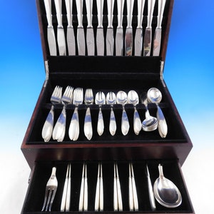 Puede incluir: Una caja de madera con un interior de terciopelo negro que contiene un juego de cubiertos de plata. La caja tiene un caj&oacute;n que contiene piezas adicionales de cubiertos.