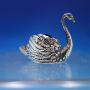 May include: A silver swan shaped ring holder. The swan has detailed feathers and a long neck.