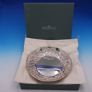 May include: A silver serving dish with an ornate design, in a white cloth bag, inside a green box with the text "UNOARGENTO" on the lid.