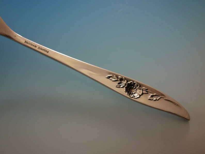 May include: Close-up of a silver fork with a floral design and the inscription "Heirloom Sterling" on the handle.