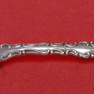 May include: A silver oyster fork with a decorative handle. The fork has two prongs and a rounded, oval-shaped bowl.