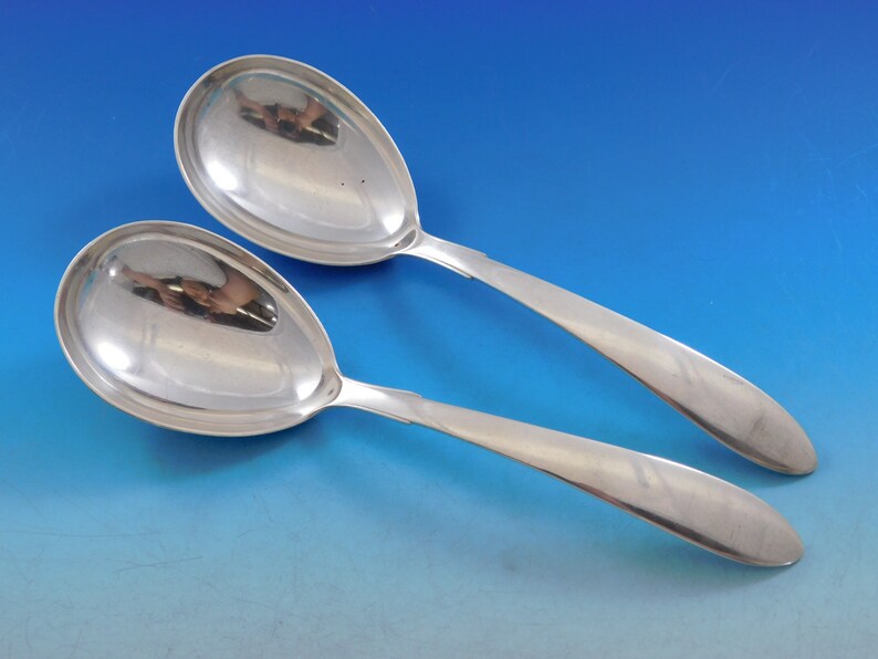 Puede incluir: Dos cucharas de servir de plata con acabado pulido. Las cucharas tienen un cuenco redondeado y un mango largo y delgado.