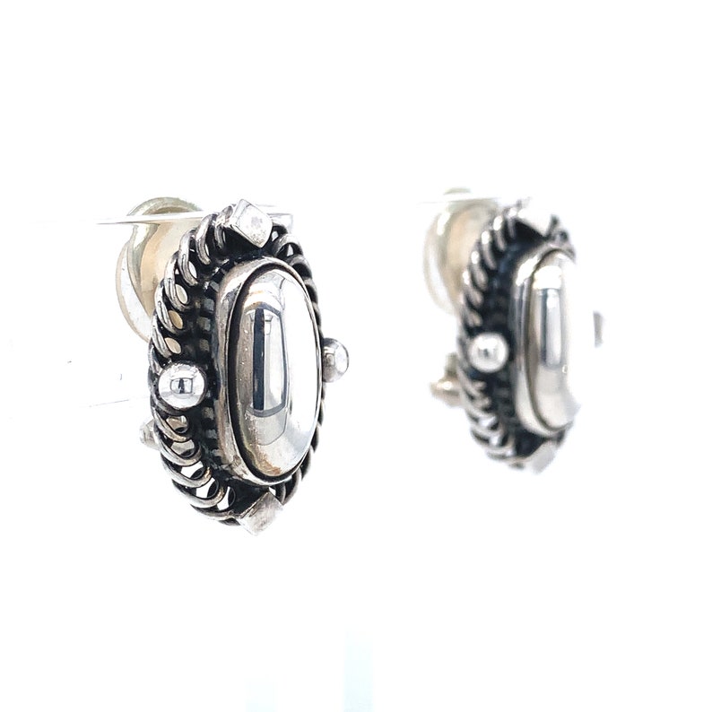 Puede incluir: Un par de pendientes de plata con un dise&ntilde;o ovalado detallado. Los pendientes tienen una superficie lisa y reflectante y un borde texturizado.