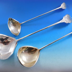 May include: Three silver serving ladles with ornate handles. The ladles are of different sizes and have a polished finish.