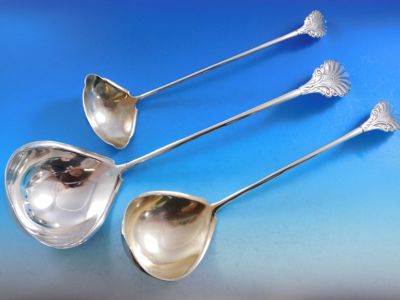 May include: Three silver serving ladles with ornate handles. The ladles are of different sizes and have a polished finish.