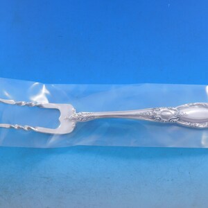 May include: A silver serving fork with a decorative handle and two prongs. The fork is packaged in a clear plastic bag.
