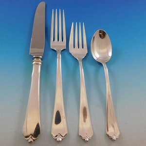 May include: A set of four silver-plated flatware pieces, including a knife, fork, teaspoon, and a larger fork. The pieces have a simple, elegant design with a scalloped edge and a rounded handle.