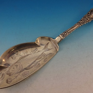 May include: A silver fish serving spoon with an ornate handle and a detailed fish design on the bowl.