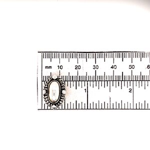 Puede incluir: Un medall&oacute;n ovalado de plata con un camafeo blanco en su interior. El medall&oacute;n mide aproximadamente 3,8 cm de largo y se mide con una regla.