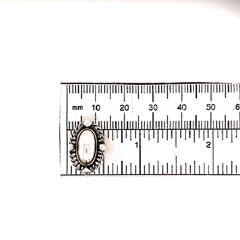 Puede incluir: Un medall&oacute;n ovalado de plata con un camafeo blanco en su interior. El medall&oacute;n mide aproximadamente 3,8 cm de largo y se mide con una regla.